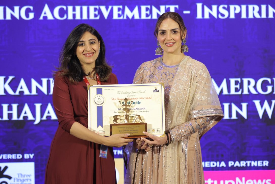 Two women standing side by side, one holding a framed certificate and a trophy presenting it to other at excellency iconic awards. Both are smiling and dressed in formal attire.