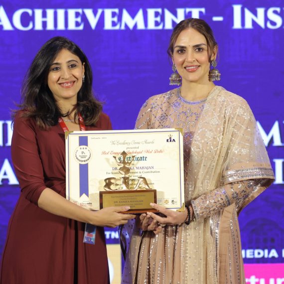 Two women standing side by side, one holding a framed certificate and a trophy presenting it to other at excellency iconic awards. Both are smiling and dressed in formal attire.